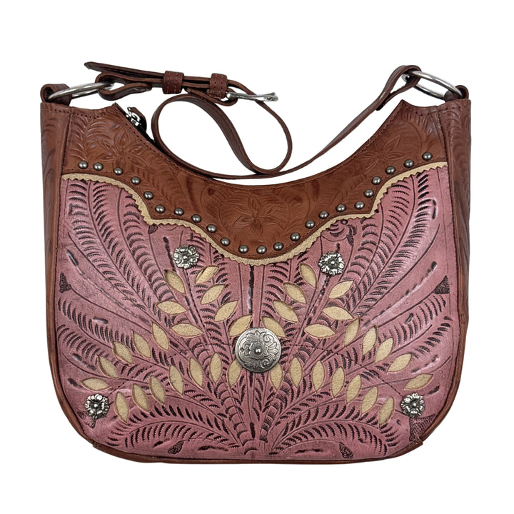 A western-style shoulder bag made of tooled leather in dusty pink and brown, decorated with silver studs, a central silver concho, and floral cutouts, shown on a plain white background.