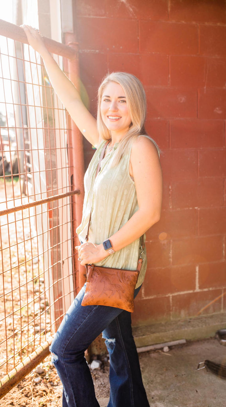 Lifestyle of crossbody/hip bag in distressed charcoal brown with hand tooled leather accents with model wearing it hooked to belt loops