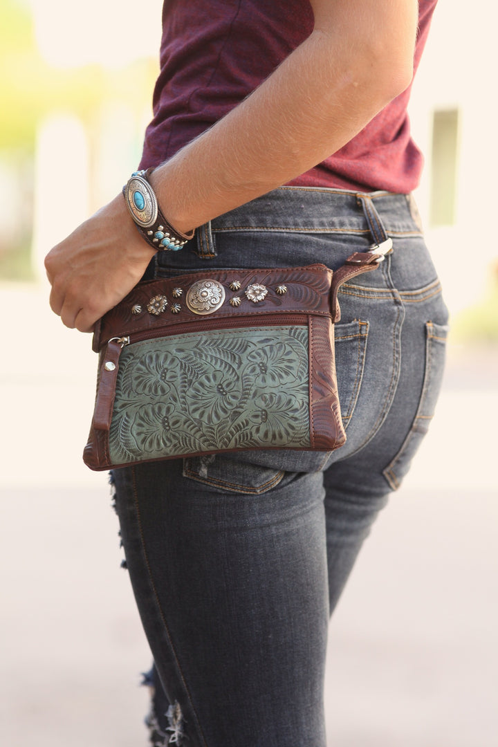 Lifestyle of crossbody/hip bag with hand tooled leather accents with model wearing it hooked to belt loops