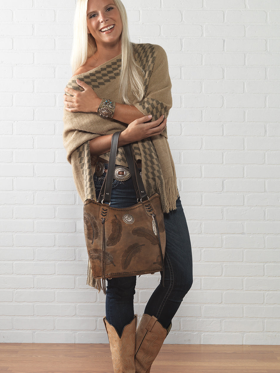Lifestyle with model of Sacred Bird bucket tote in distressed charcoal brown leather with hand tooled feathers
