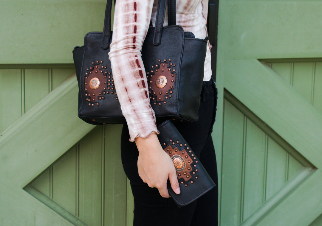 Lifestyle with model of Midnight Copper tri-fold wallet in black accents shown with matching handbag
