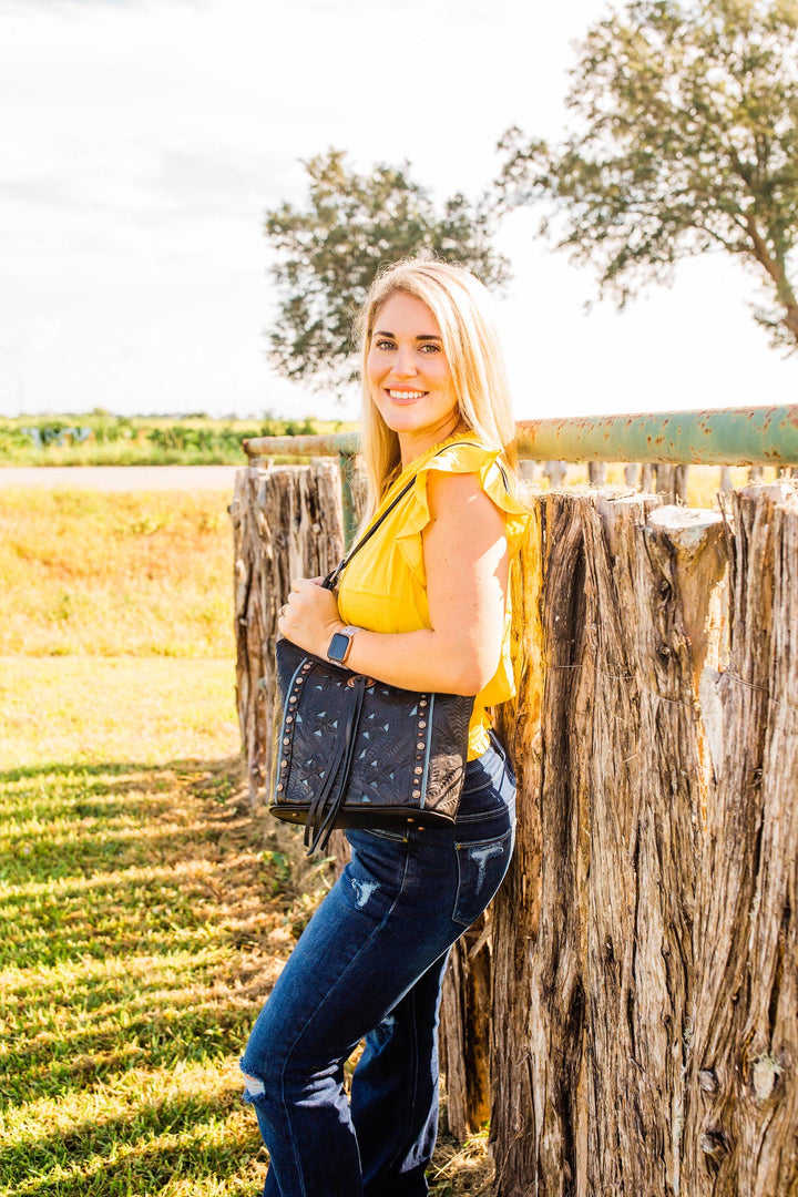 Lifestyle with model of Hill Country bucket tote in black with hand tooled leather accents and bolo concho with tassel