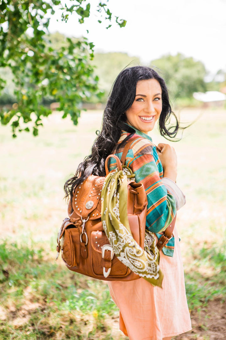 Lifestyle with model of Classic Travel drawstring backpack with front pocket in medium brown with hand tooled leather and buckle set accents