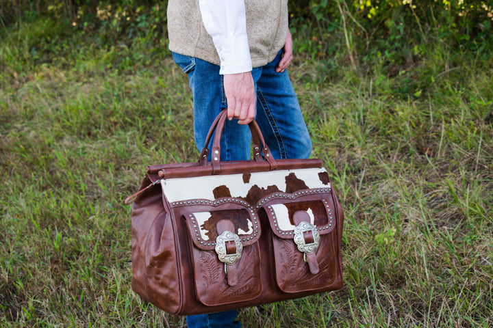 Lifestyle with model of Cowtown duffel bag with front pockets in dark brown with hand tooled leather and hair-on hide accents